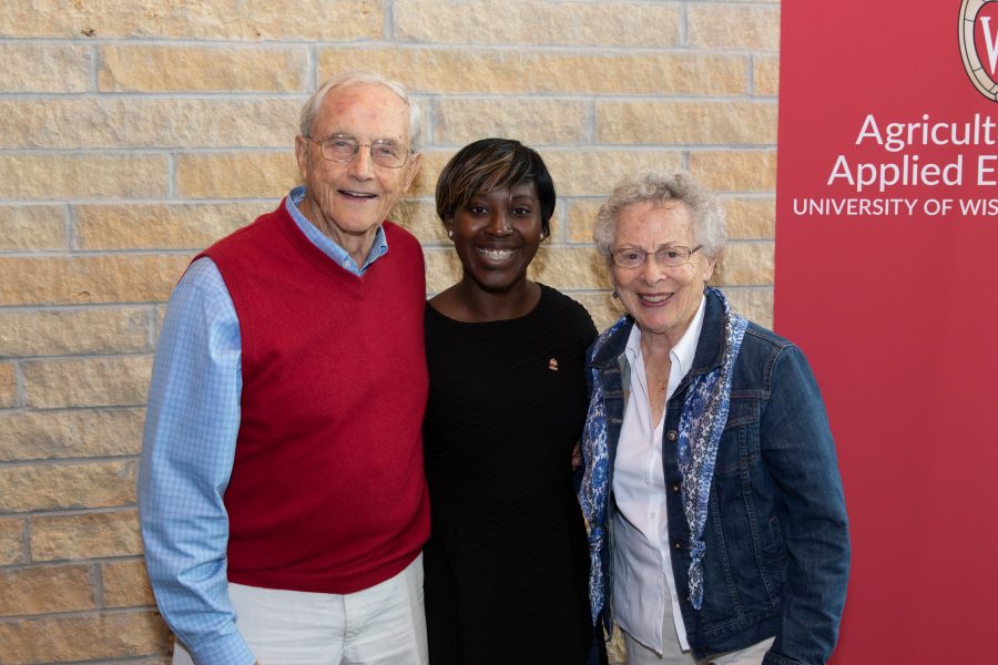two alumni with student in front of banner
