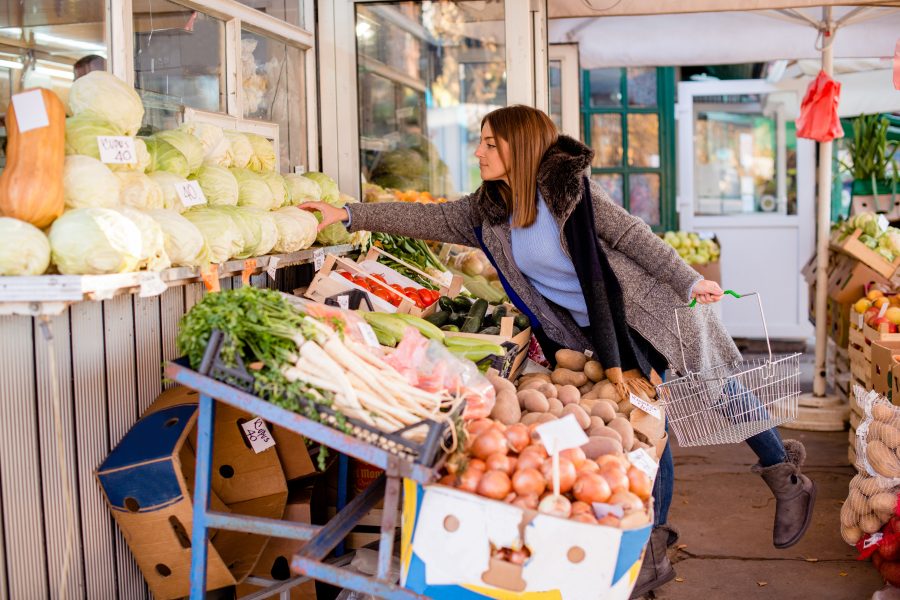 Young woman picking cabbage at farmer`s market, various vegetables at market stall.